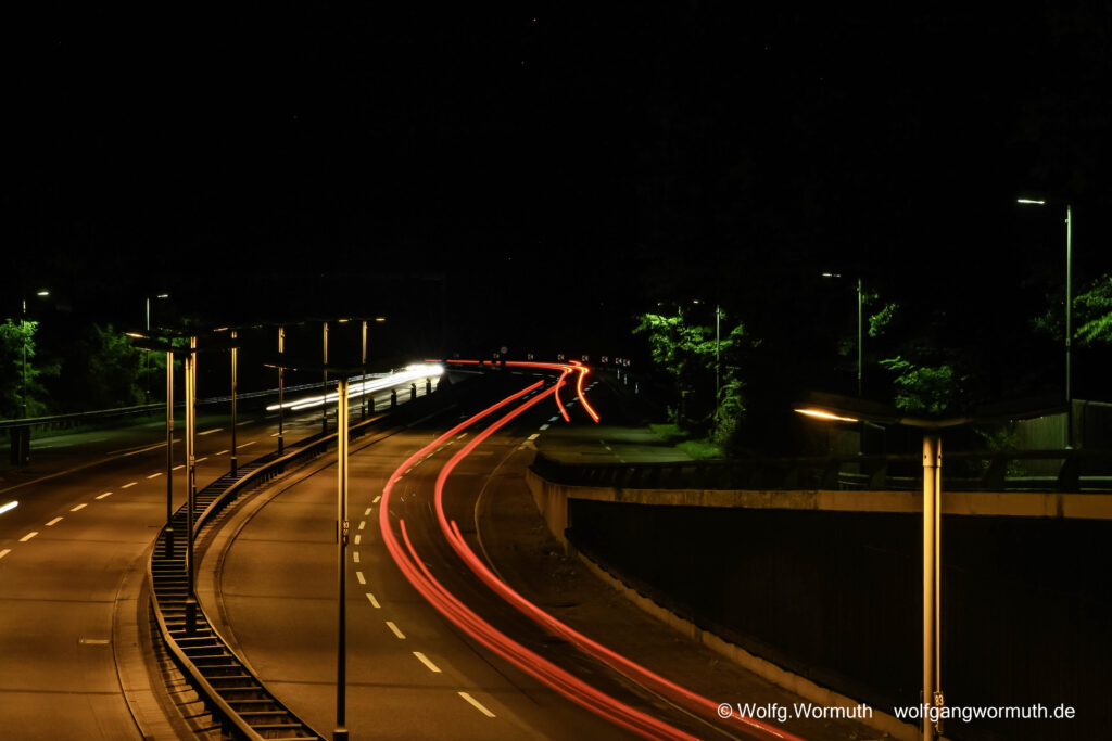 Nachtaufnahme von Autobahnbrücke Heiligensee. Scheinwerfer und Rücklichter bilden weiße und rote Streifen in der Kurve.